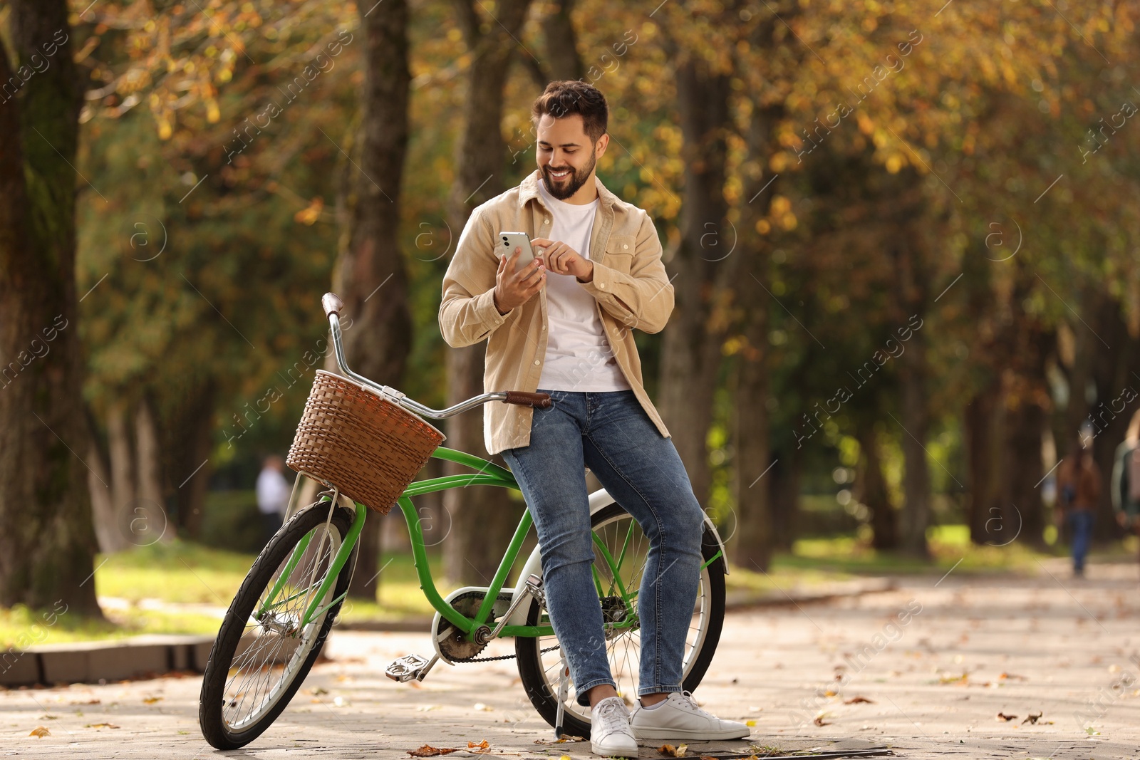 Photo of Young man with bicycle using smartphone in autumn park, space for text