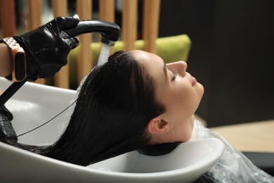 Photo of Hairdresser rinsing out dye from woman's hair in beauty salon