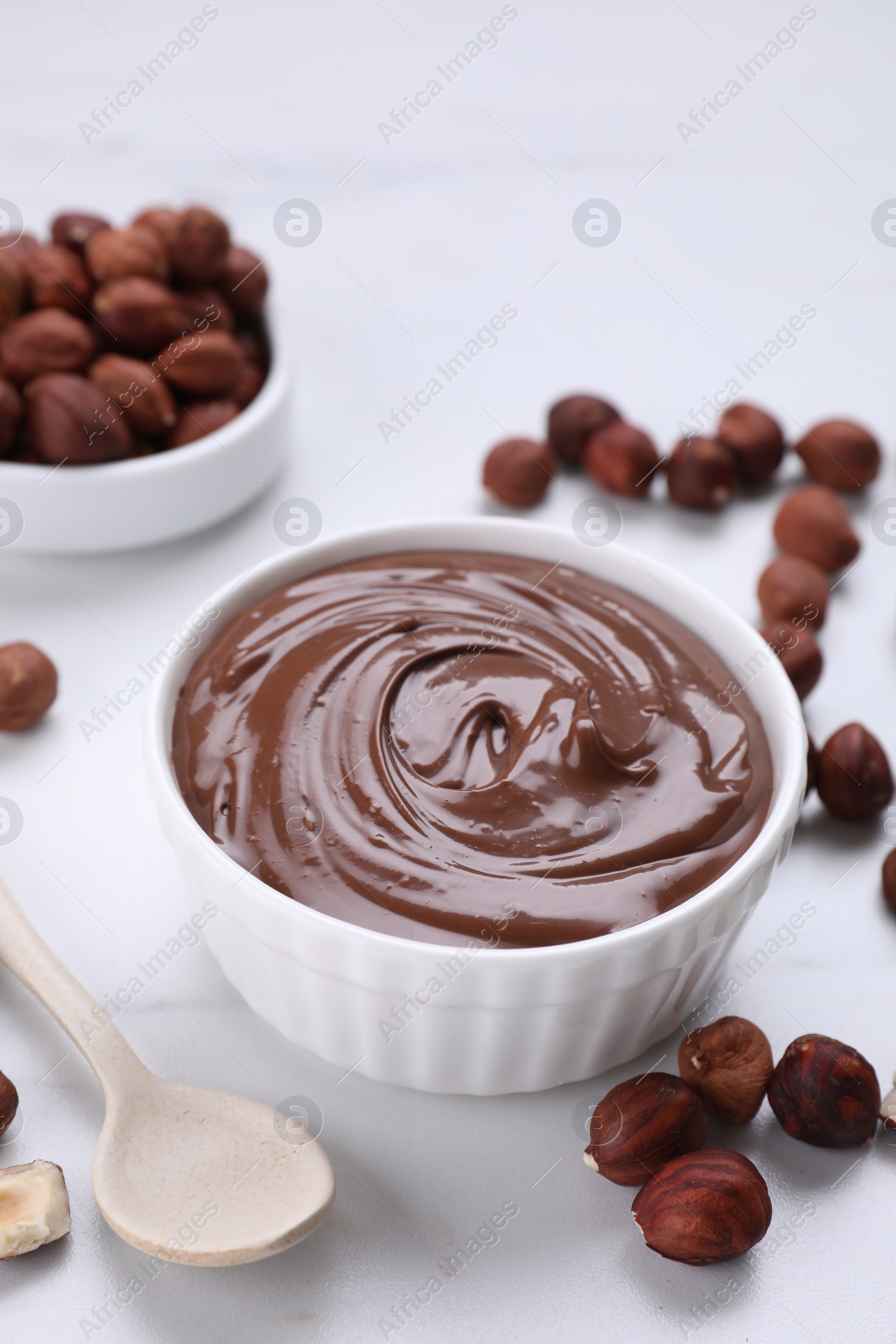 Photo of Bowl with chocolate paste and nuts on white marble table