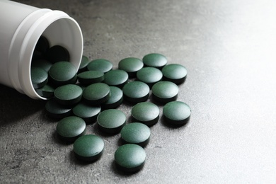 Photo of Plastic container with green spirulina pills on grey table