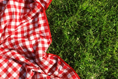 Checkered picnic tablecloth on fresh green grass, top view. Space for text