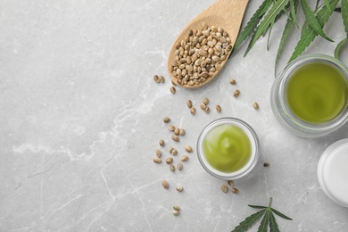 Jars of hemp cream and seeds on grey table, flat lay with space for text. Organic cosmetics