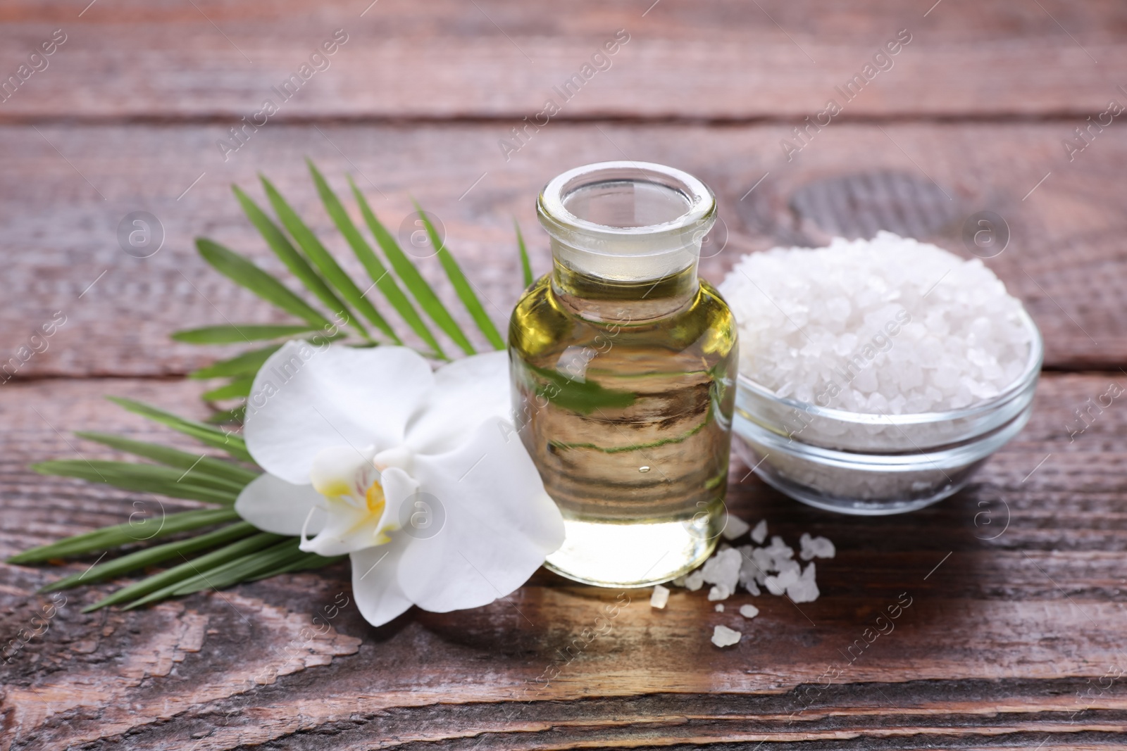 Photo of Bottle of essential oil, sea salt and orchid flower on wooden table, closeup