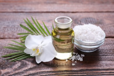 Photo of Bottle of essential oil, sea salt and orchid flower on wooden table, closeup