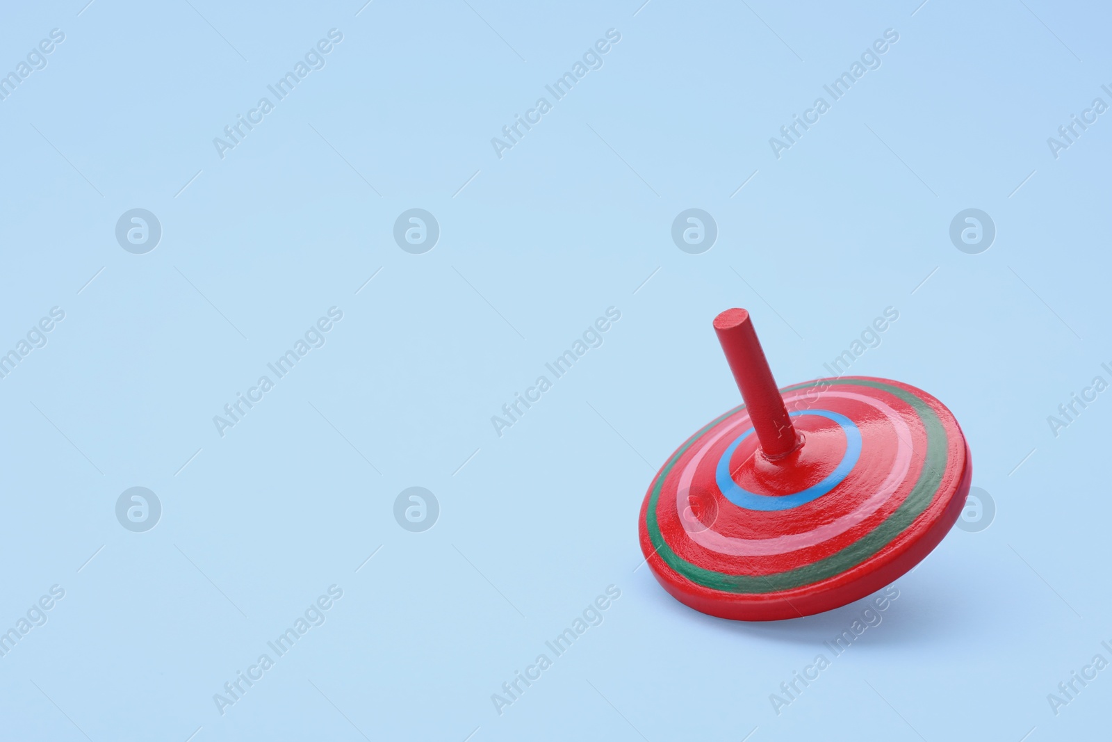 Photo of One bright spinning top on light blue background, space for text. Toy whirligig