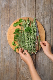 Woman with rosemary and other herbs on wooden background, top view