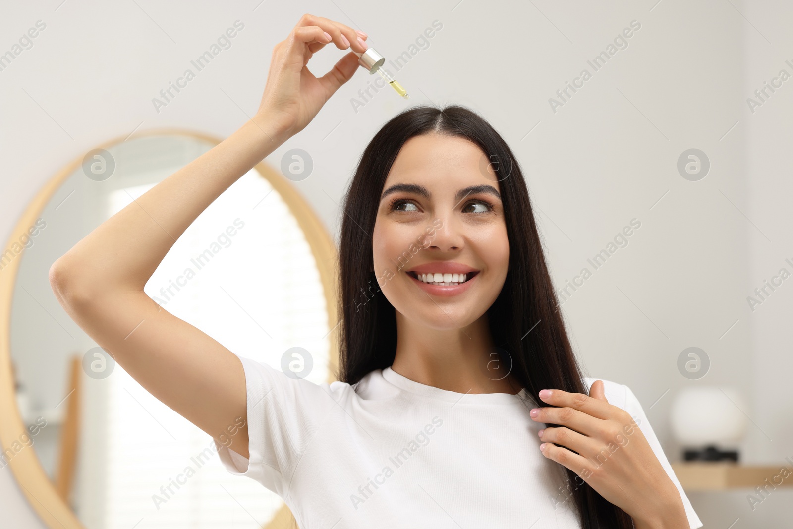 Photo of Beautiful woman applying hair serum in bathroom. Cosmetic product