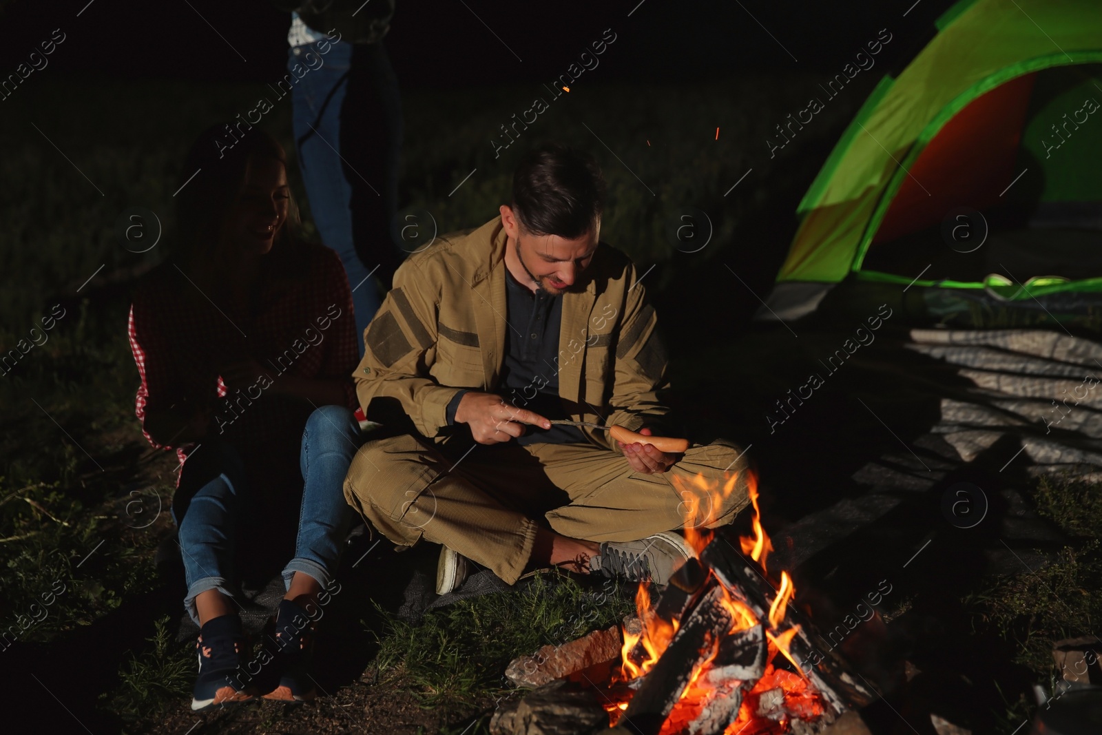 Photo of Young friends spending time near bonfire at night. Camping season