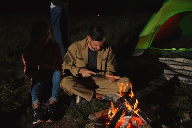 Young friends spending time near bonfire at night. Camping season