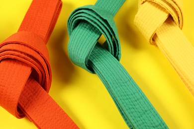 Photo of Colorful karate belts on yellow background, closeup
