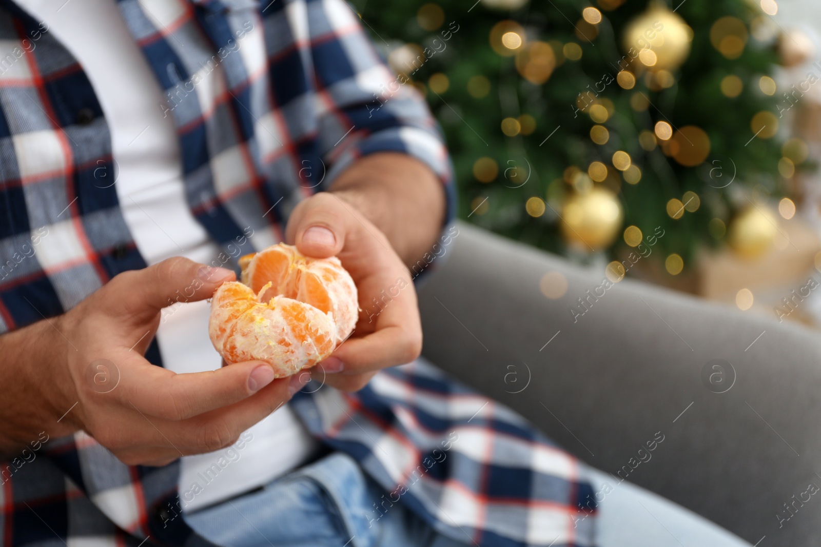 Photo of Man with peeled tangerine near Christmas tree, closeup