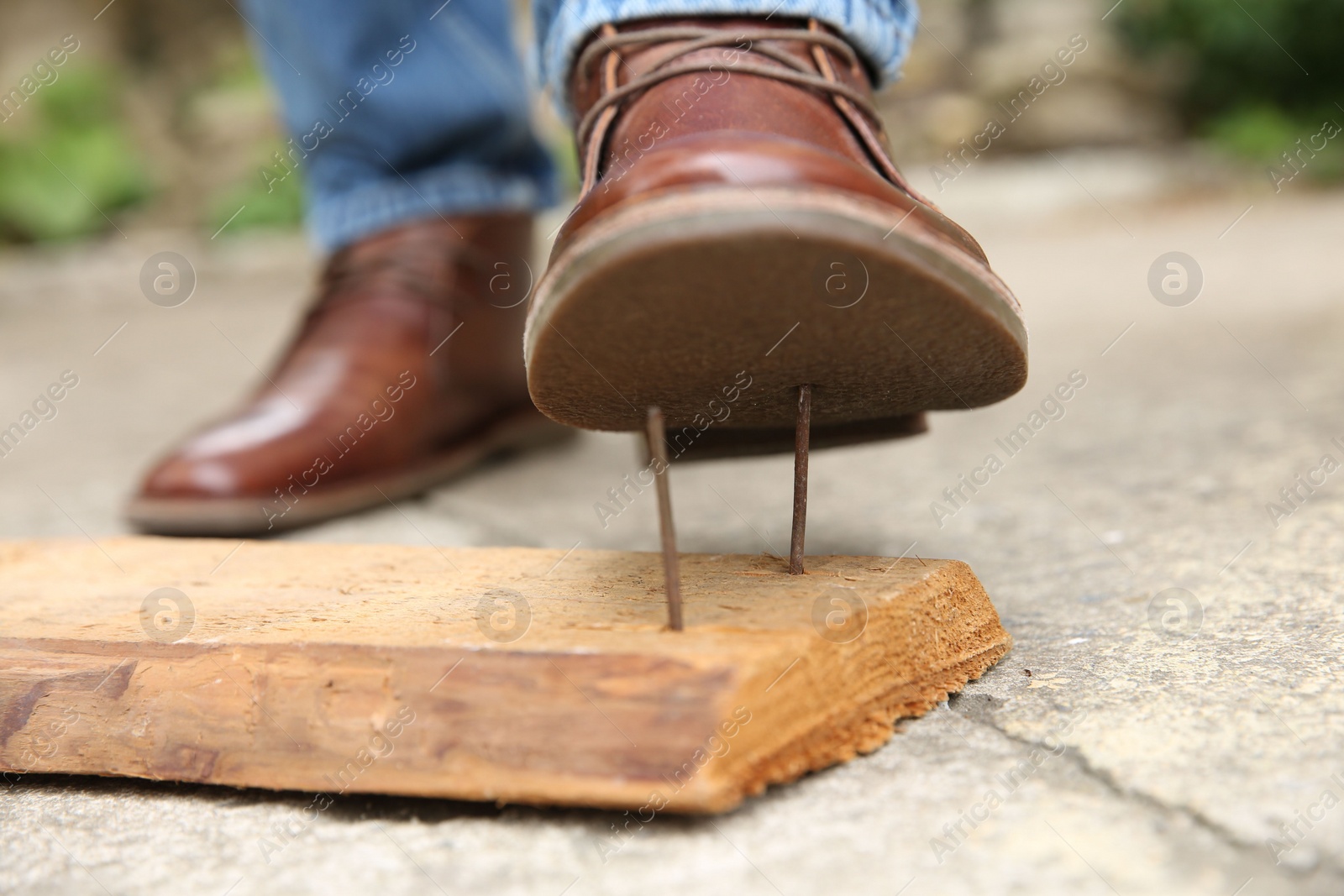 Photo of Careless man stepping on nails in wooden plank outdoors, closeup