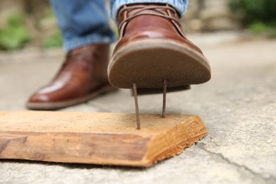 Photo of Careless man stepping on nails in wooden plank outdoors, closeup