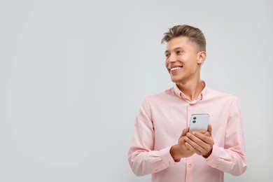 Happy young man sending message via smartphone on light grey background. Space for text
