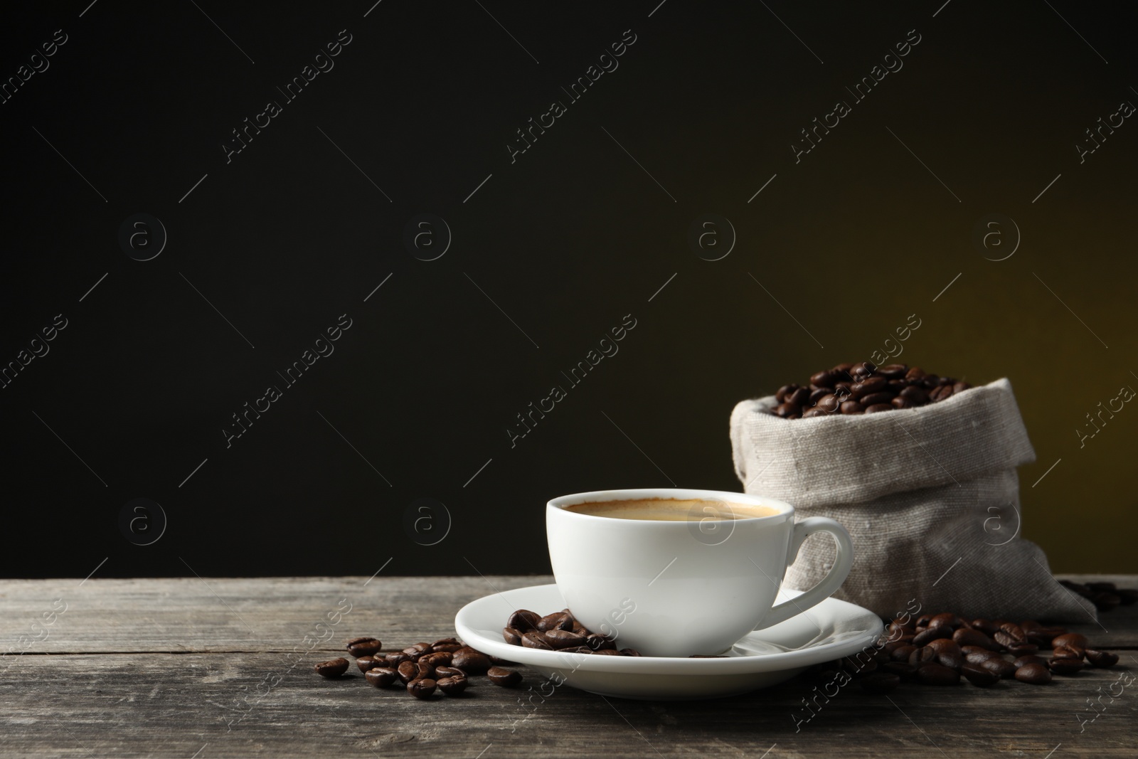 Photo of Cup of hot aromatic coffee and roasted beans on wooden table against dark background, space for text