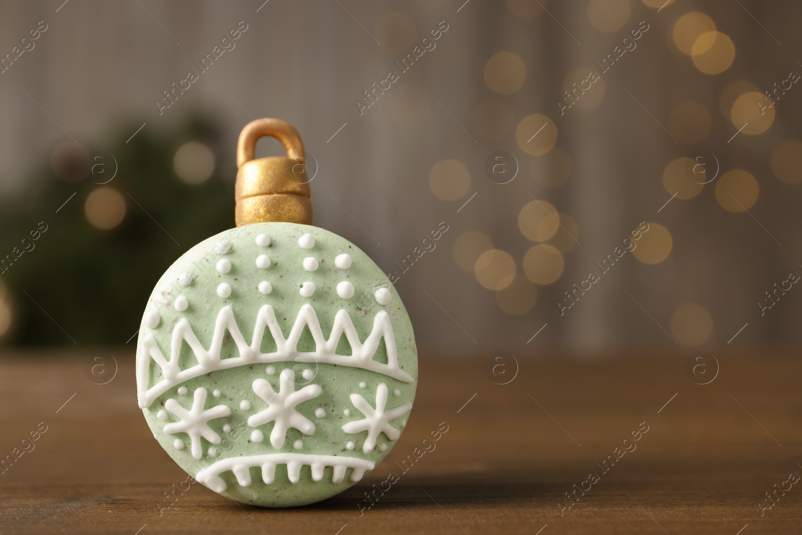 Photo of Beautifully decorated Christmas macaron on wooden table against blurred festive lights, space for text