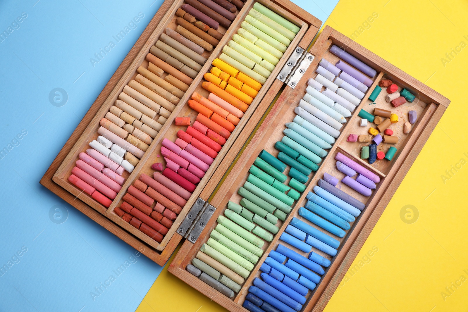 Photo of Drawing pastel set in wooden box on color background, top view