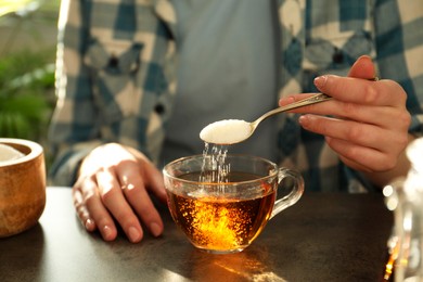 Woman adding sugar into cup of tea at dark table, closeup