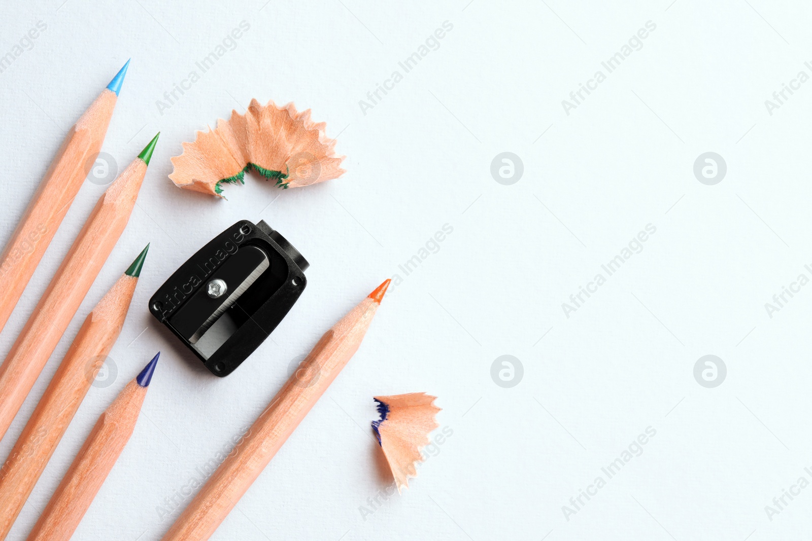 Photo of Colorful pencils, sharpener and shavings on white background, flat lay. Space for text