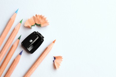 Photo of Colorful pencils, sharpener and shavings on white background, flat lay. Space for text