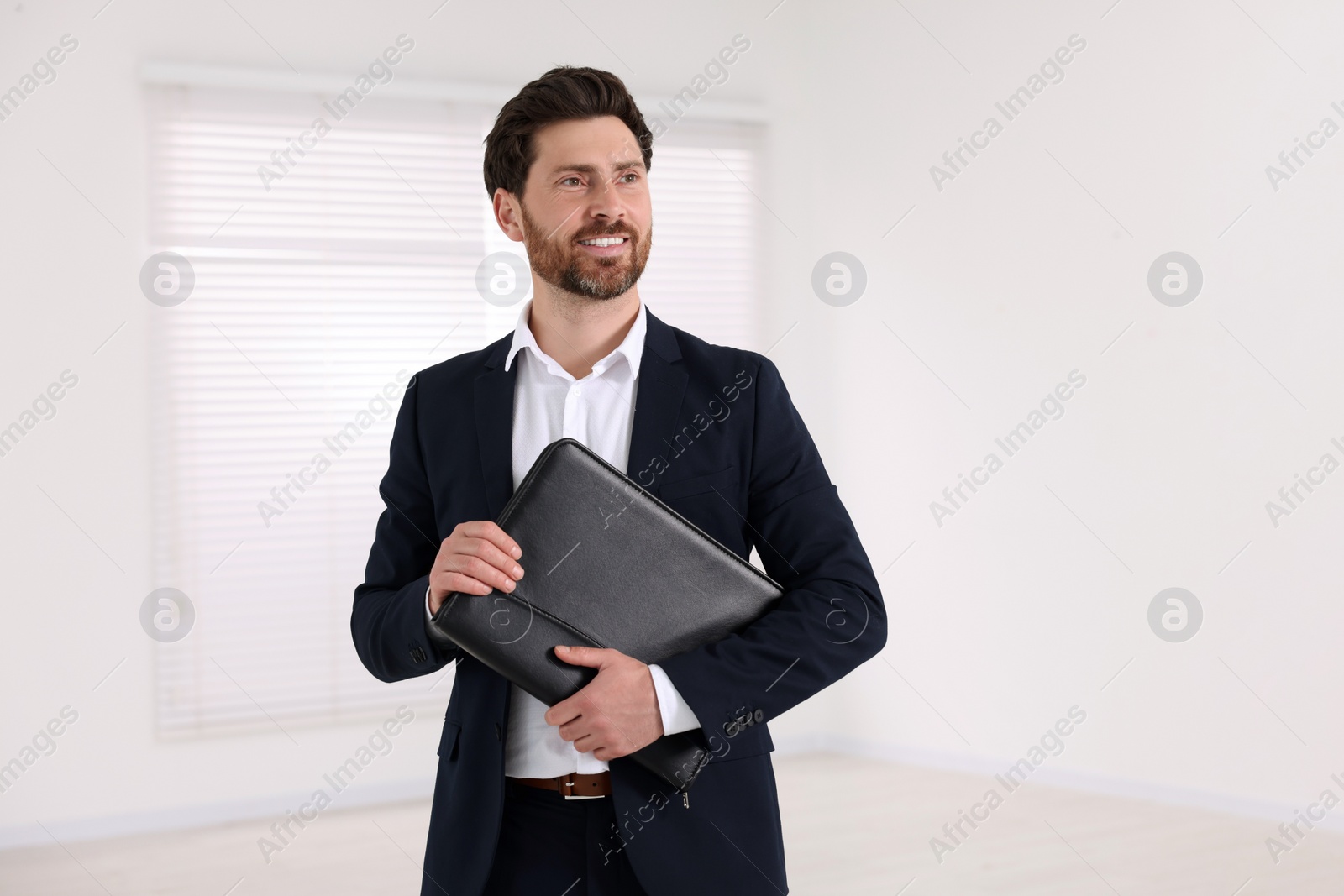 Photo of Happy real estate agent with leather portfolio indoors. Space for text