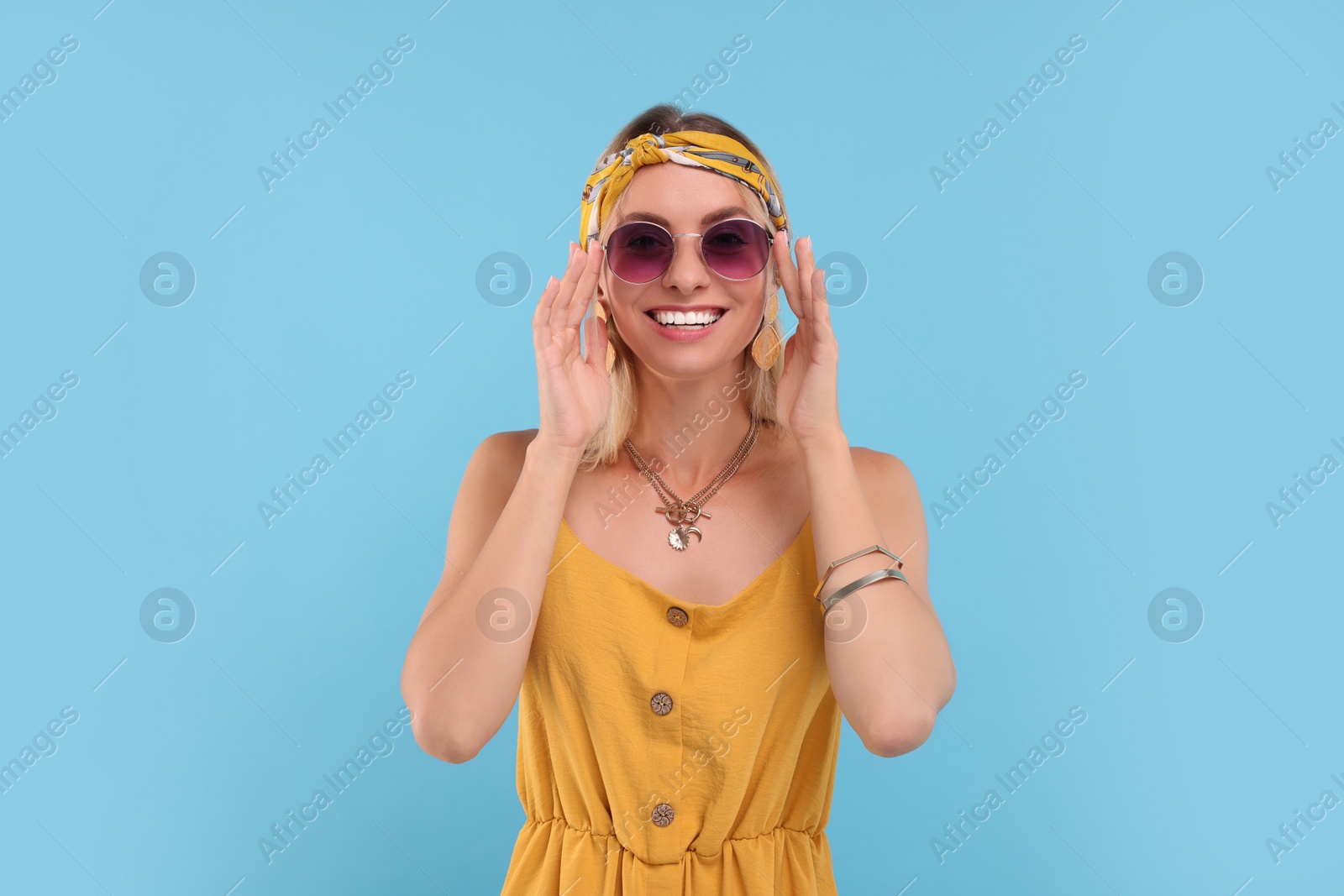 Photo of Portrait of smiling hippie woman in sunglasses on light blue background