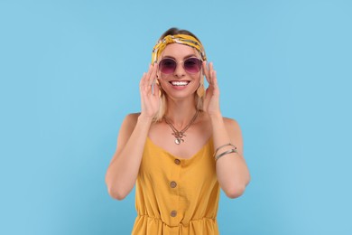 Portrait of smiling hippie woman in sunglasses on light blue background
