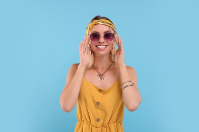 Photo of Portrait of smiling hippie woman in sunglasses on light blue background