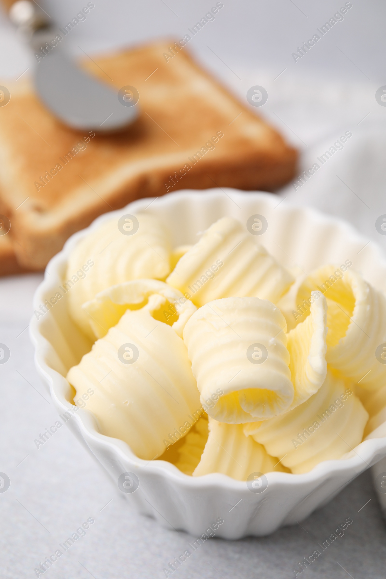 Photo of Tasty butter curls in bowl on light grey table, closeup