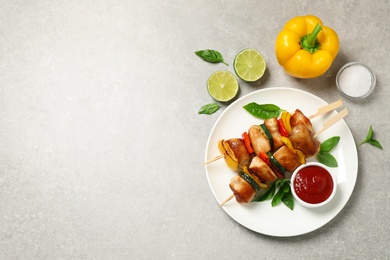 Photo of Delicious chicken shish kebabs with vegetables and ketchup on grey table, flat lay. Space for text