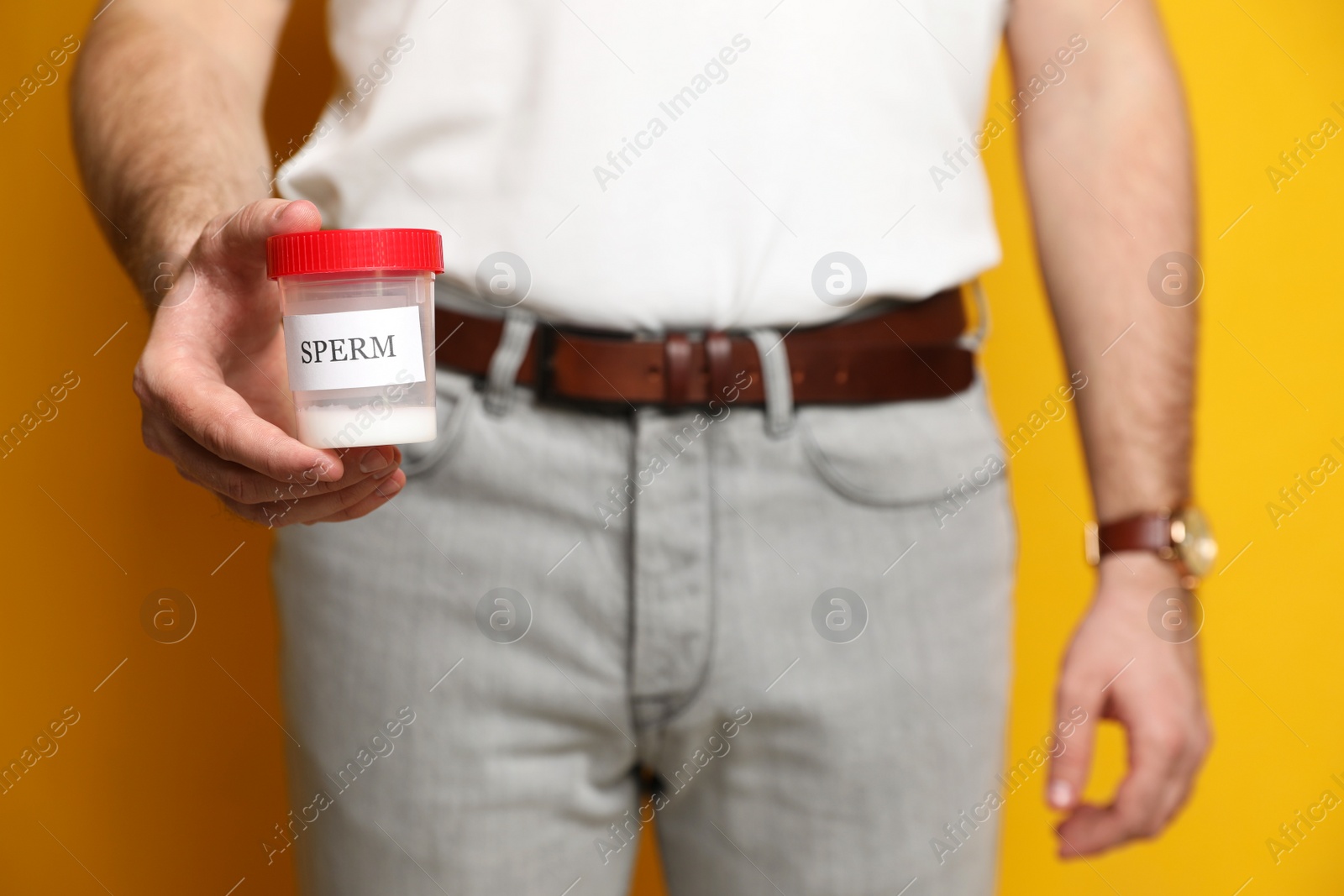 Photo of Donor holding container with sperm on yellow background, closeup