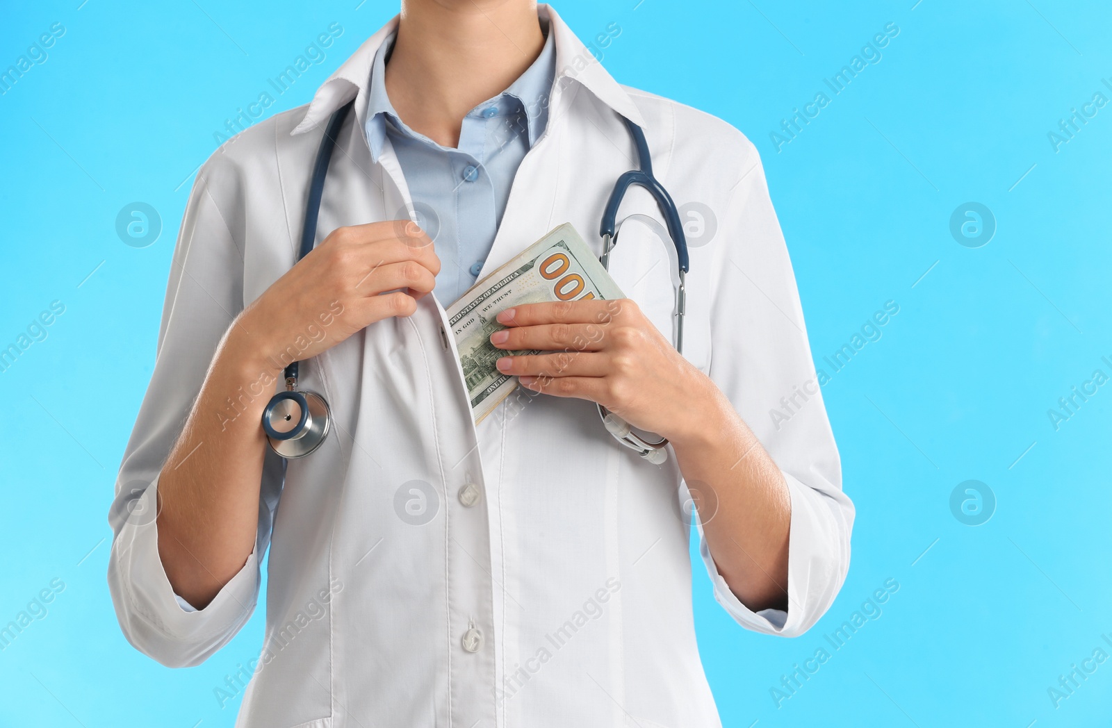 Photo of Doctor putting bribe money into pocket on light blue background, closeup. Corruption in medicine