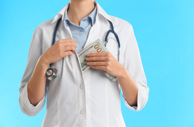 Doctor putting bribe money into pocket on light blue background, closeup. Corruption in medicine