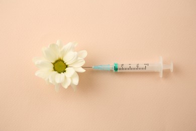 Medical syringe and beautiful chrysanthemum flower on beige background, top view