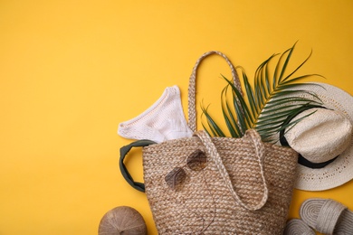 Stylish straw bag and summer accessories on yellow background, flat lay