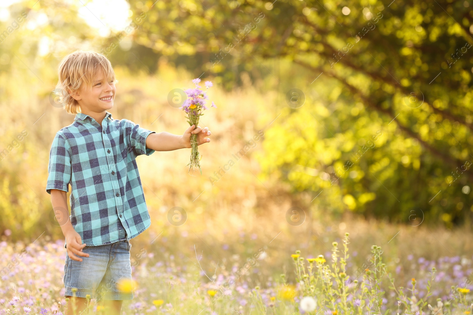 Photo of Cute little boy with bouquet of wildflowers outdoors, space for text. Child spending time in nature