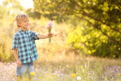 Photo of Cute little boy with bouquet of wildflowers outdoors, space for text. Child spending time in nature