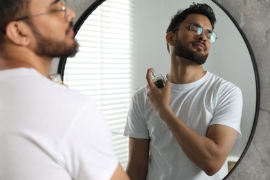 Man spraying luxury perfume near mirror indoors