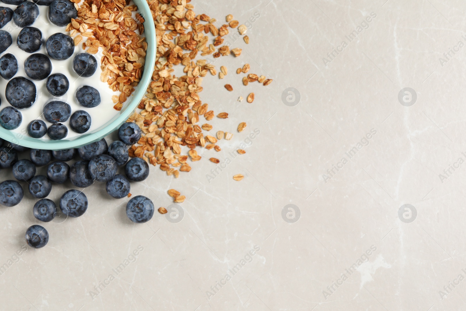 Photo of Bowl of yogurt with granola and blueberries on grey marble table, flat lay. Space for text