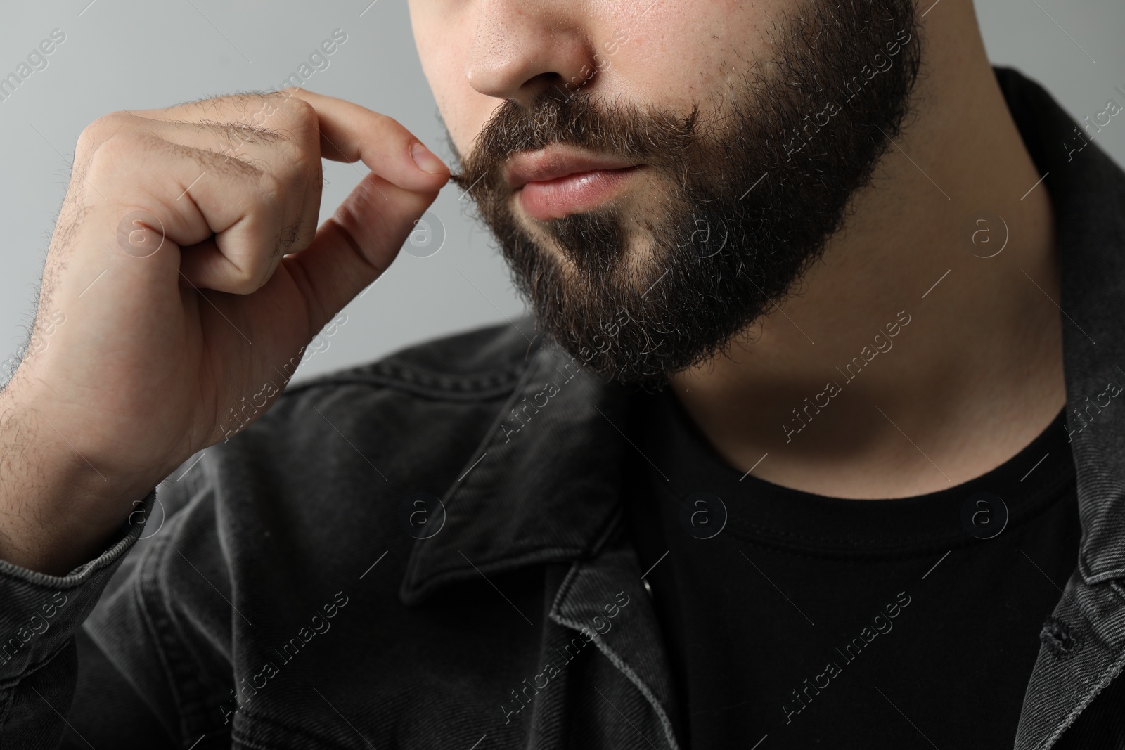 Photo of Young man touching mustache on grey background, closeup