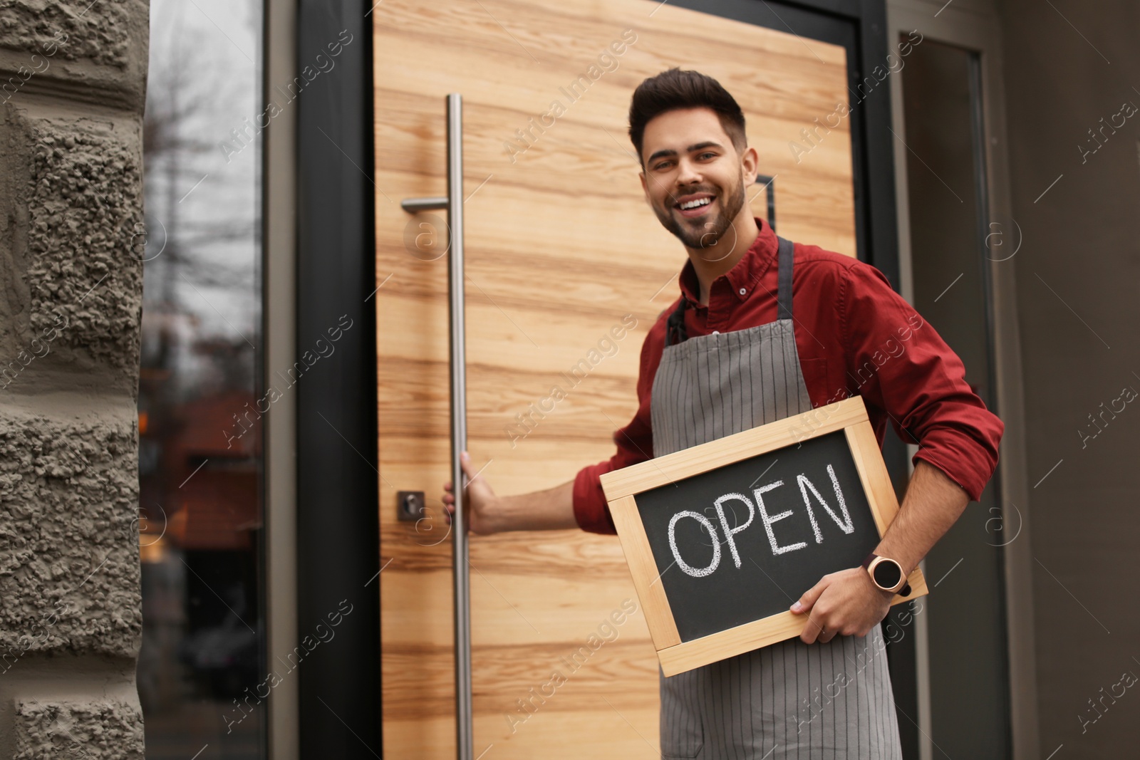 Photo of Young male business owner holding OPEN sign near his cafe. Space for text
