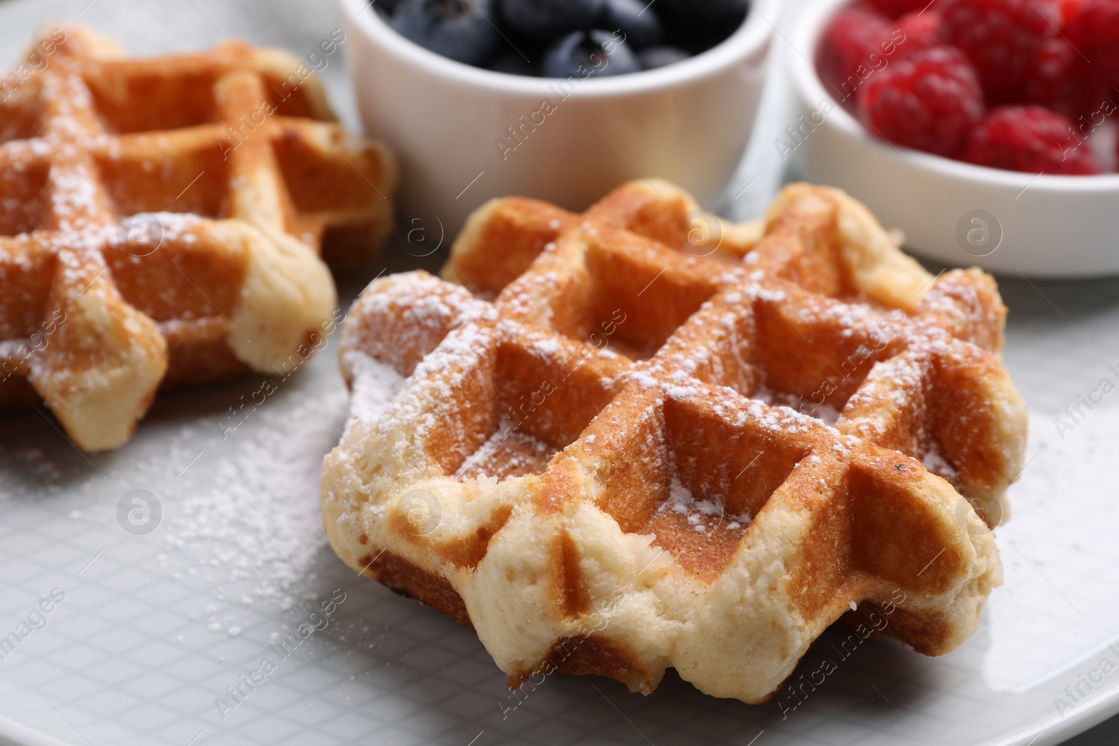 Photo of Delicious Belgian waffles with fresh berries and powdered sugar on plate, closeup