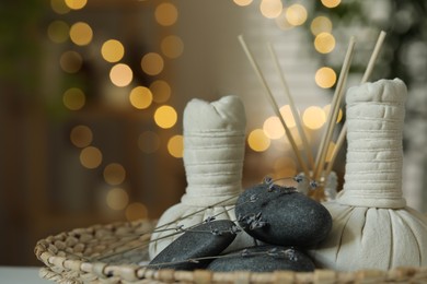 Photo of Spa composition. Herbal bags, stones, reed diffuser and dry lavender flowers in wicker tray indoors, bokeh effect