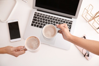 Women holding coffee cups at modern workplace in office, top view