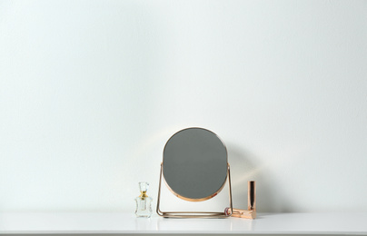 Photo of Small mirror, perfume and lipsticks on table near white wall. Space for text