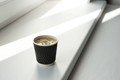 Photo of Cardboard cup of coffee on window sill indoors