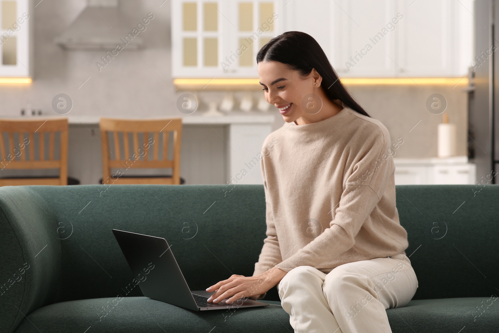 Photo of Happy woman working with laptop on sofa in kitchen