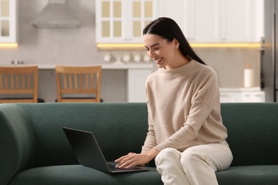 Photo of Happy woman working with laptop on sofa in kitchen