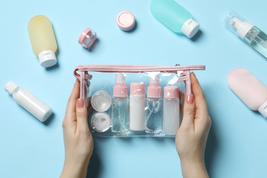 Photo of Cosmetic travel kit. Woman with plastic bag and small containers of personal care products on light blue background, top view