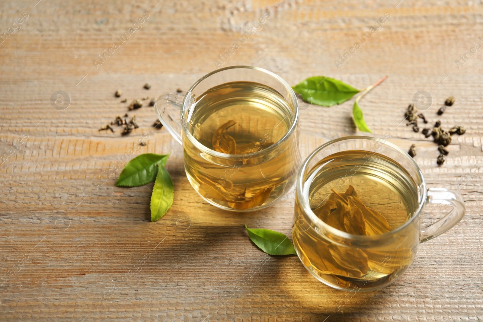 Photo of Cup of green tea, dry and fresh leaves on wooden table